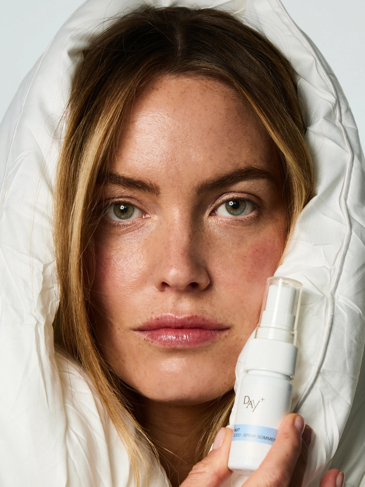 Femme enlacé dans une couette tenant dans ses mains le Spray Sommeil Dodo.