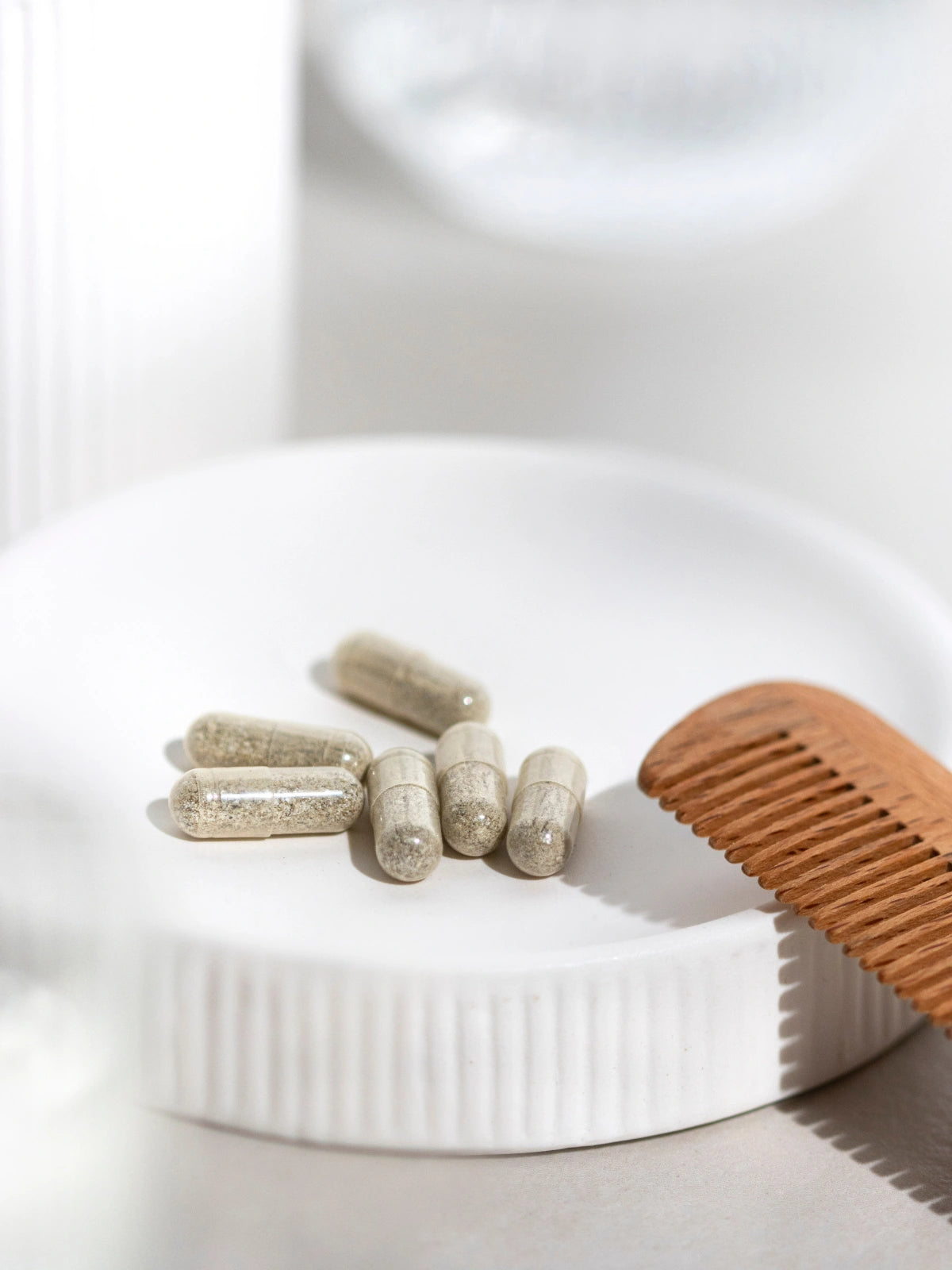 Six Gélules Cheveux Fortifiantes dans une coupelle et un peigne en bois apposé à côté.