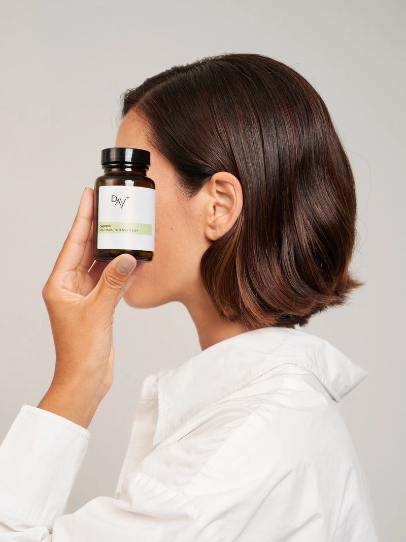 femme qui met à côté de son visage une boîte de gélules cheveux