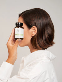 femme qui met à côté de son visage une boîte de gélules cheveux