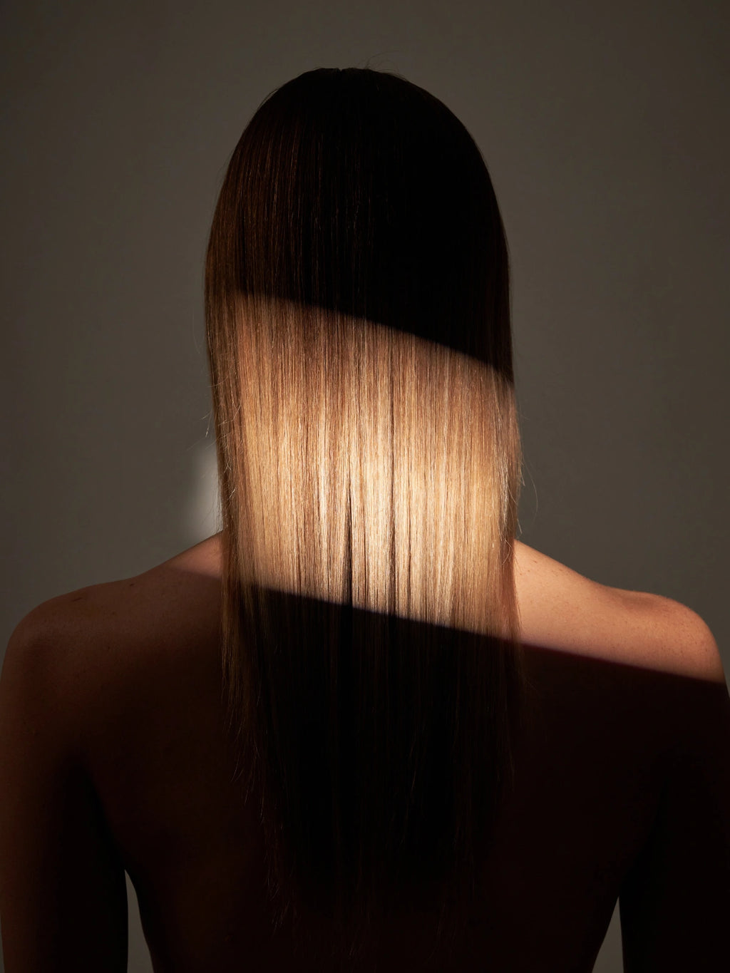 Femme aux cheveux longs de dos avec un reflet de lumière illuminant ces cheveux.