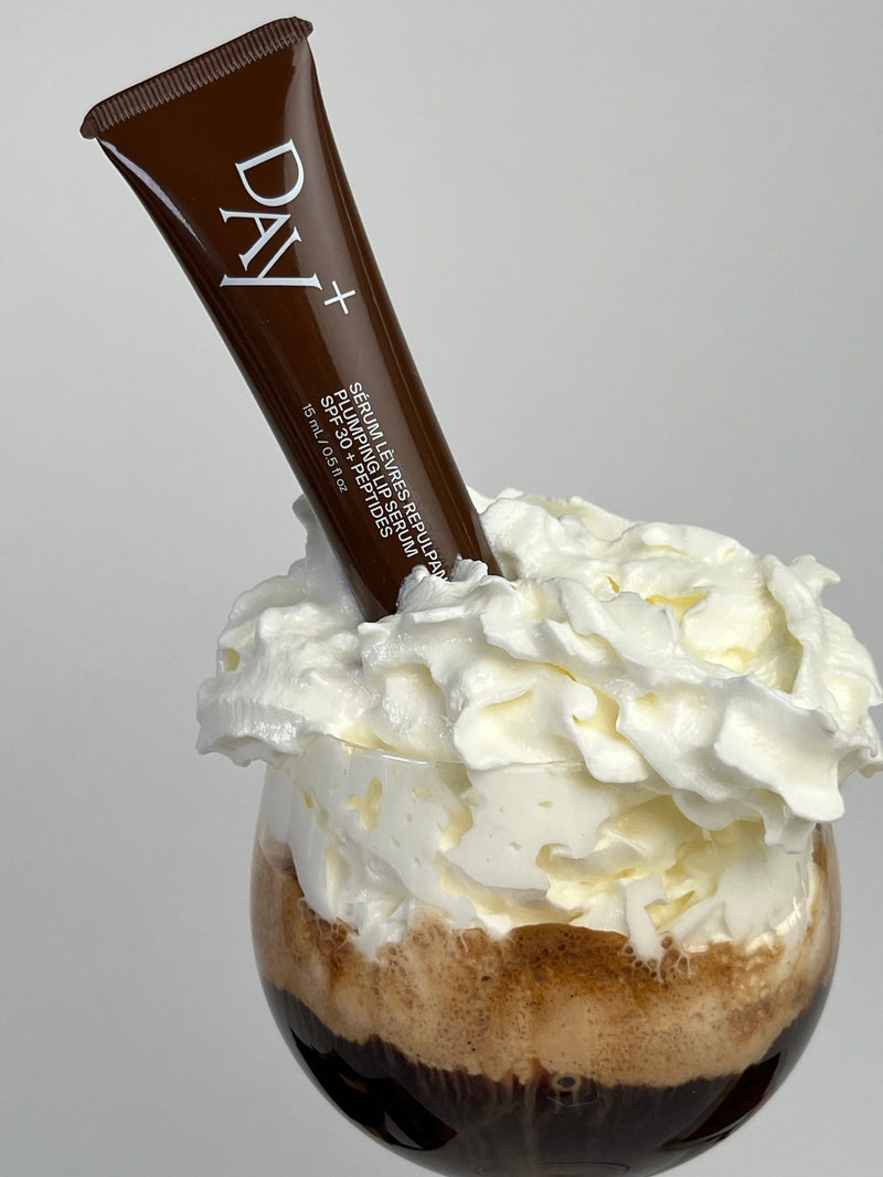 Le Sérum Lèvres Repulpant chocolat planté dans la chantilly d'un café.