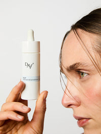 Femme de profil tenant le Sérum Nuit Régénérant Intense face à elle.