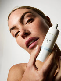 Femme tenant le Sérum Nuit Régénérant Intense près de son visage.