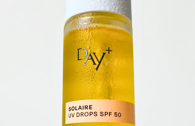 Zoom sur le flacon du sérum solaire UV Drops SPF 50, avec un effet mouillé.
