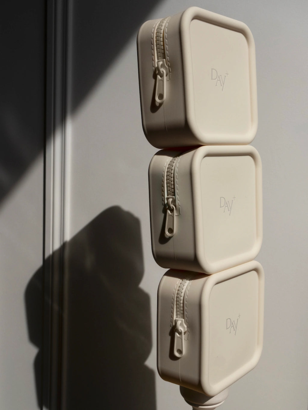 Photo de 3 trousses beige de voyage Day+ empilées les unes sur les autres.