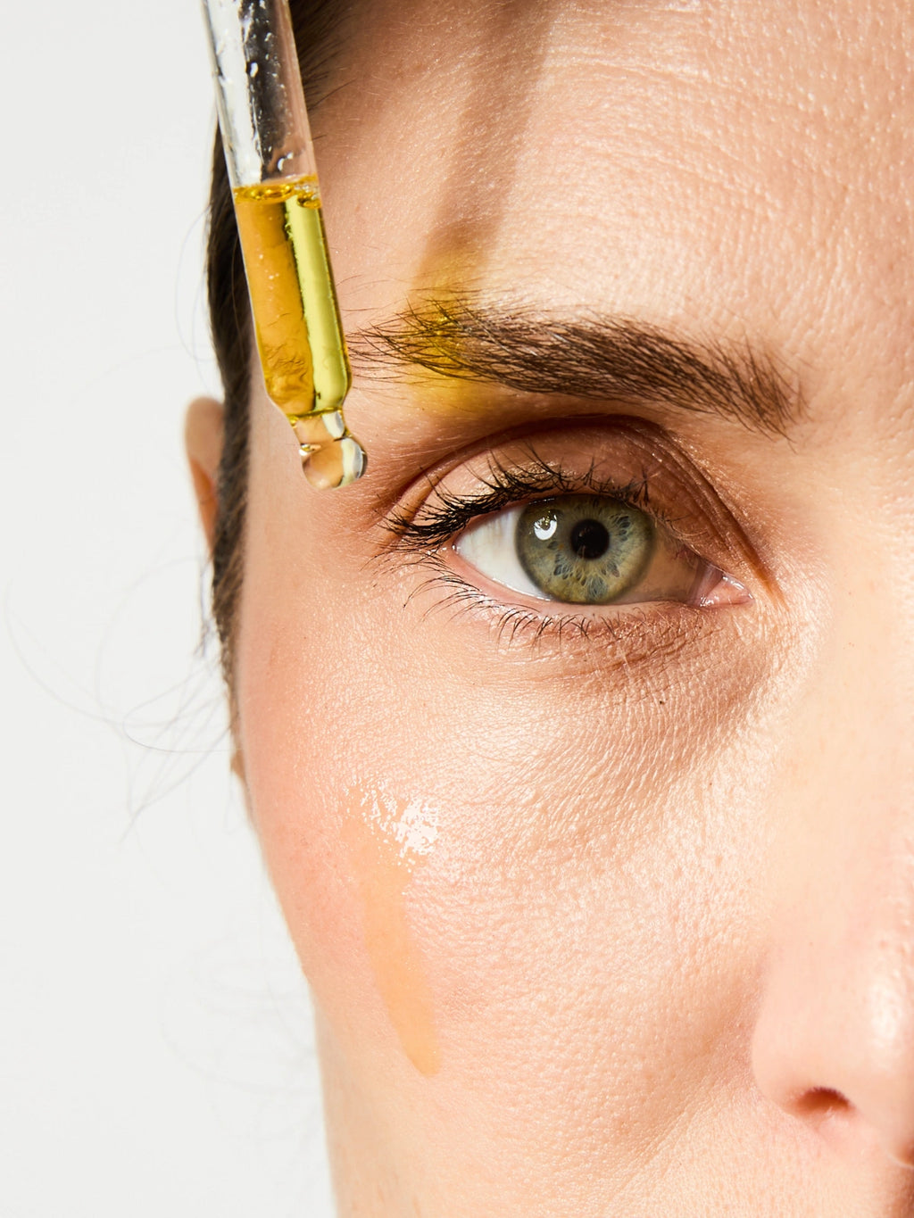 Pipette des UV Drops SPF 50 sur le visage d'une femme.