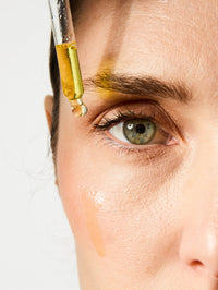 Pipette des UV Drops SPF 50 sur le visage d'une femme.