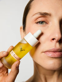 Femme tenant le Sérum solaire UV Drops SPF 50 près de son visage.