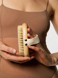 Prise en main de la Brosse Corps Day+ par sa lanière beige.