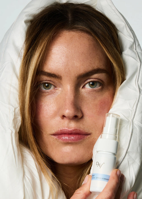 Femme enlacé dans une couette tenant dans ses mains le Spray Sommeil Dodo.