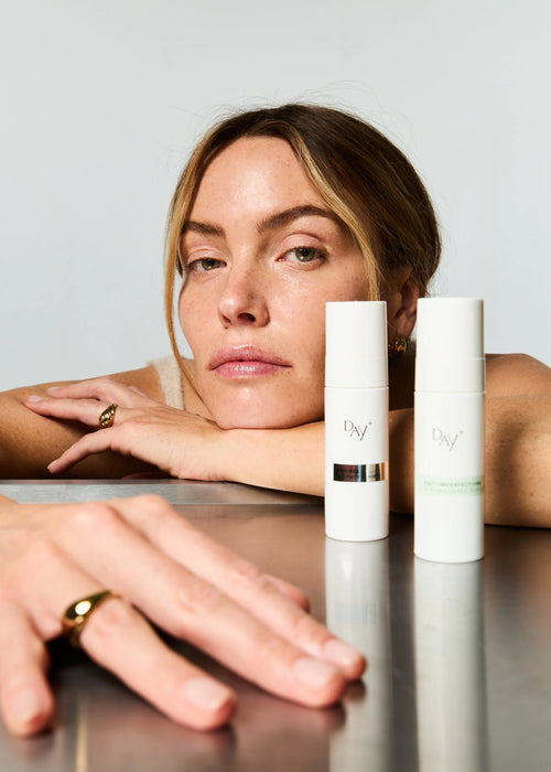 Duo de Sérums Anti-âge et Anti-imperfections posé sur une table sur laquelle est accoudée une femme.