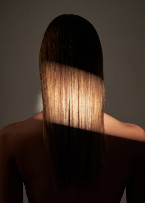 Femme aux cheveux longs de dos avec un reflet de lumière illuminant ces cheveux.
