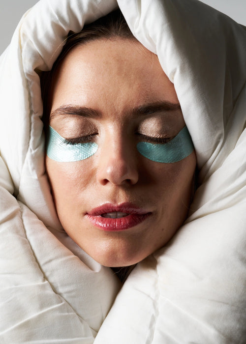 Femme portant les Patchs Yeux Régénérants Nuit enroulée dans une couette.