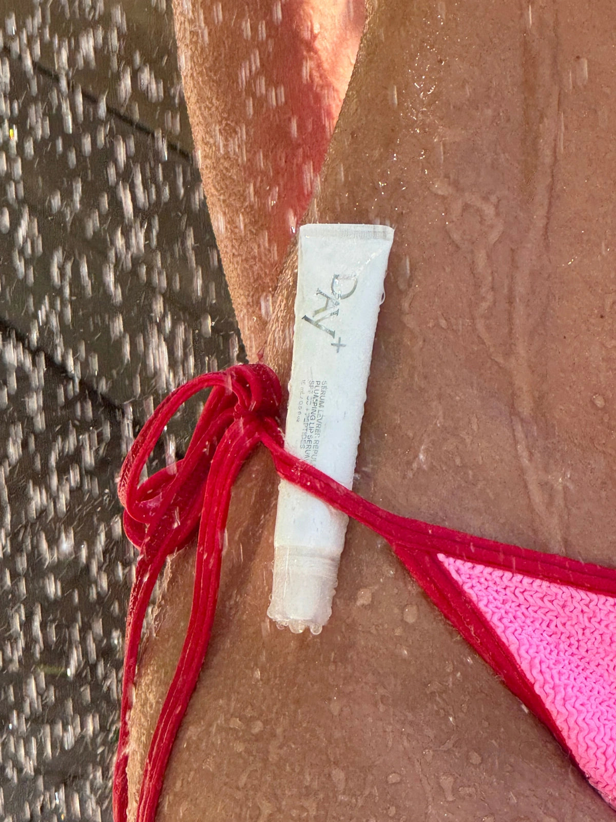Sérum Lèvres Repulpant en teinte 03. Glitter All Over coincé dans un maillot de bain sous une douche en bord de piscine.