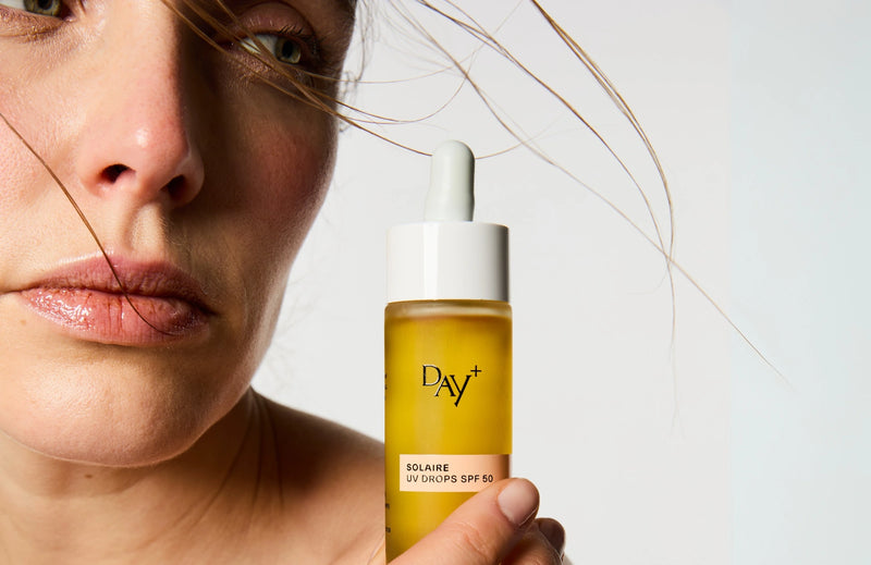 Femme tenant par dessus son épaule le sérum UV Drops SPG 50.