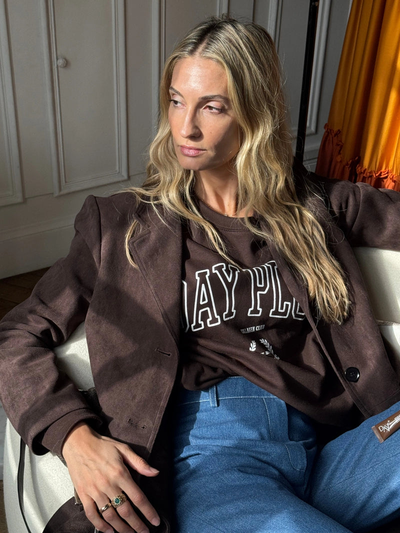 Femme assise sur un fauteuil portant le Sweatshirt Day+ University marron.