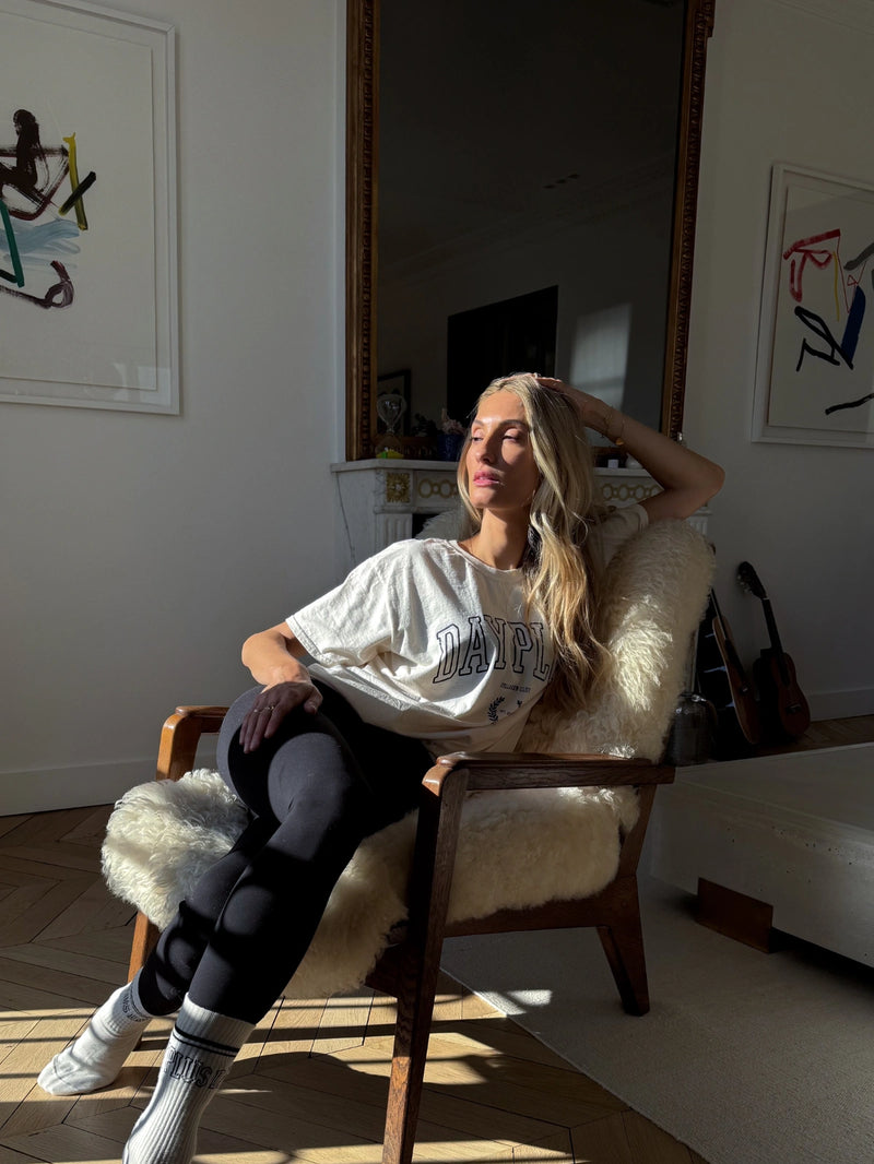 Femme assise dans un fauteuil portant le T-shirt beige de la collection capsule Day+ University.