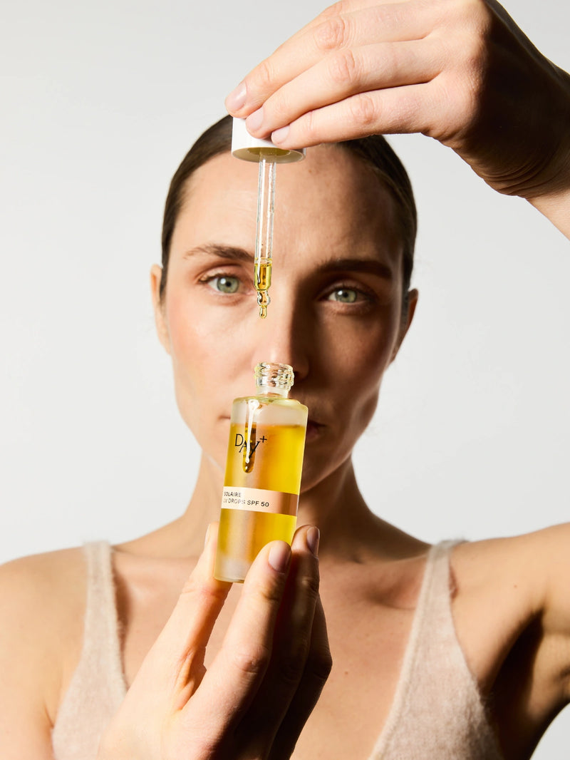 Femme faisant couler une goutte du sérum solaire SPF 50 sur le flacon.