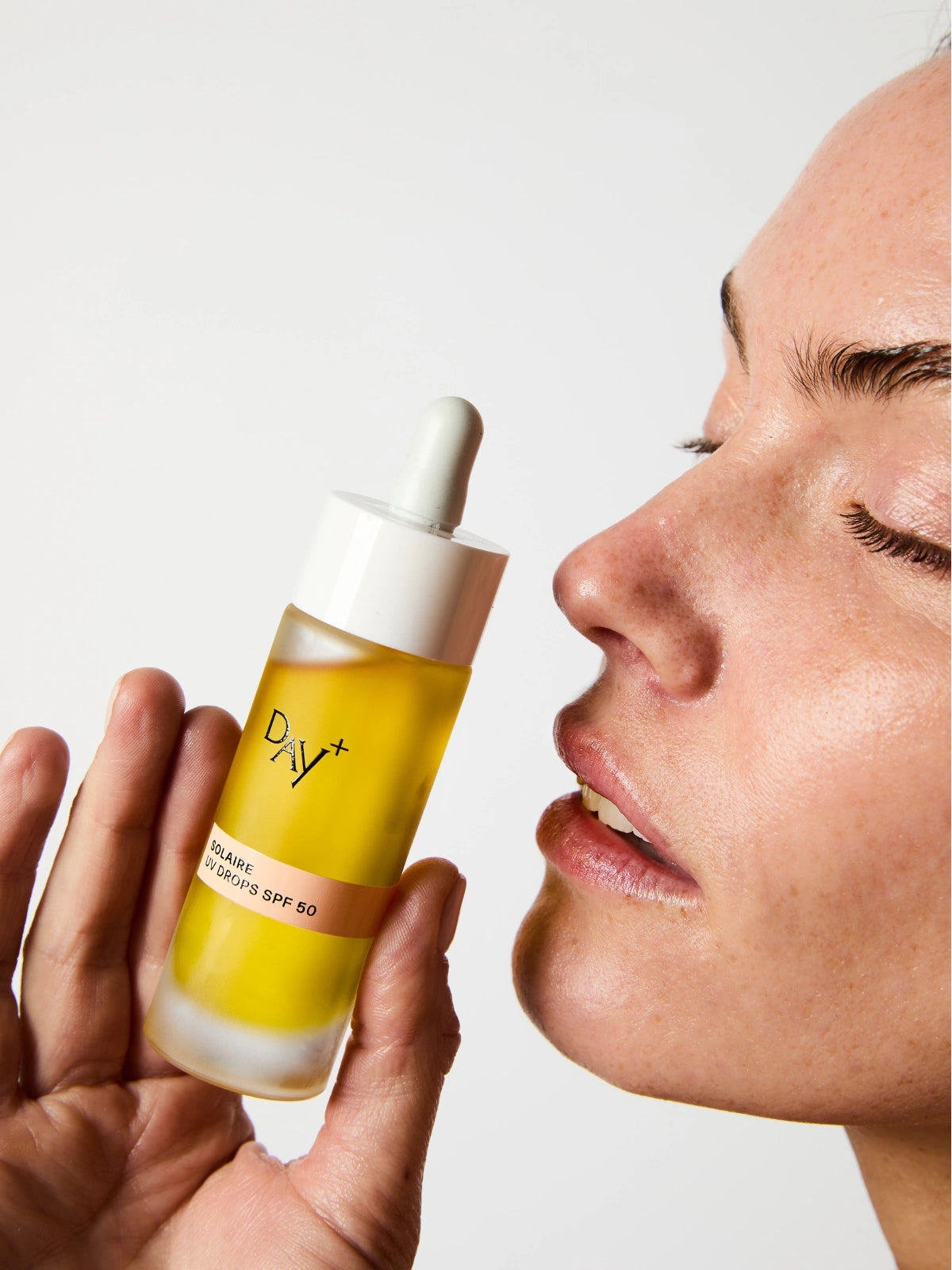 Femme tenant les UV Drops SPF 50 près de son visage.