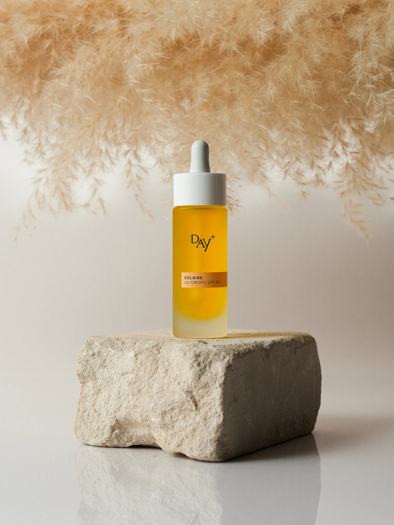 Flacon du sérum solaire UV Drops SPF 50 mis en évidence sur une pierre.
