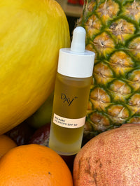 Le Sérum solaire UV Drops SPF 50 posé sur des fruits : ananas, melon et orange.